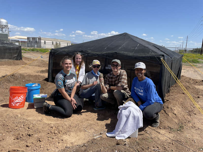 A group of five volunteers and conservationists from Wild at Heart pose in front of a newly erected tent and hold a burrowing owl up for the camera