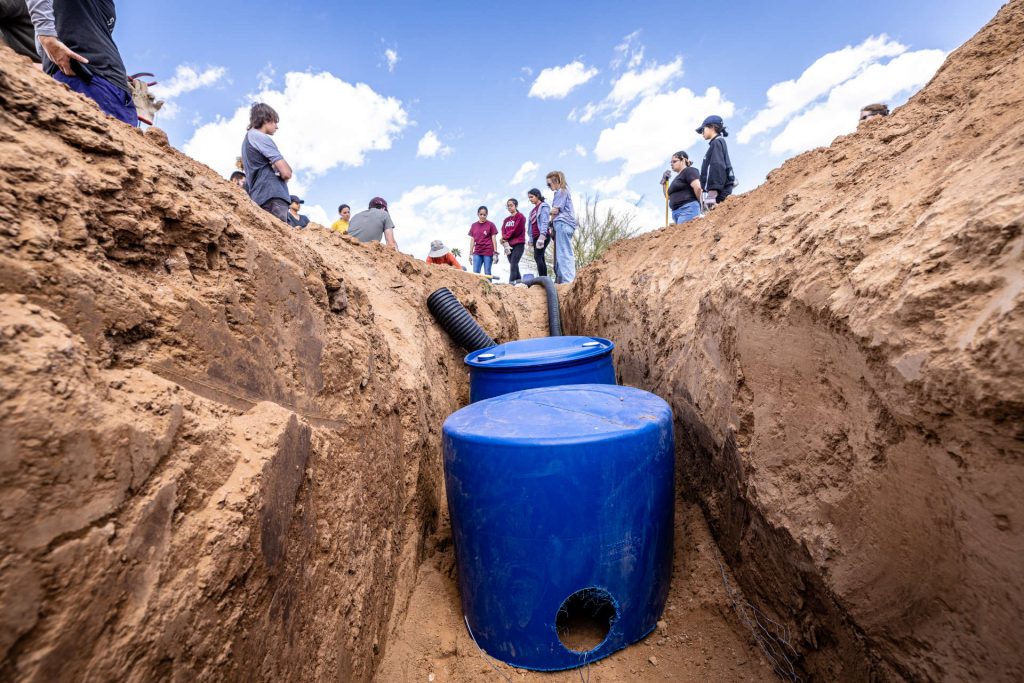 Two shelters, placed back-to-back are installed in the nearly four-foot deep trough as Wild at Heart burrowing owl habitat coordinators demonstrate for a dozen ASU Polytechnic campus students and faculty how to construct new underground shelters for relocated birds on Friday, March 24, 2023. The birds were initially translocated to the undeveloped parts of the campus in May 2021. Unseasonably heavy rains flooded the habitats. Faculty and students from the College of Integrative Sciences and Arts, Wild at Heart raptor rescue and community volunteers installed weather-proof housing for the small raptors. The group installed six shelters, with plans to return the birds over the weekend. 