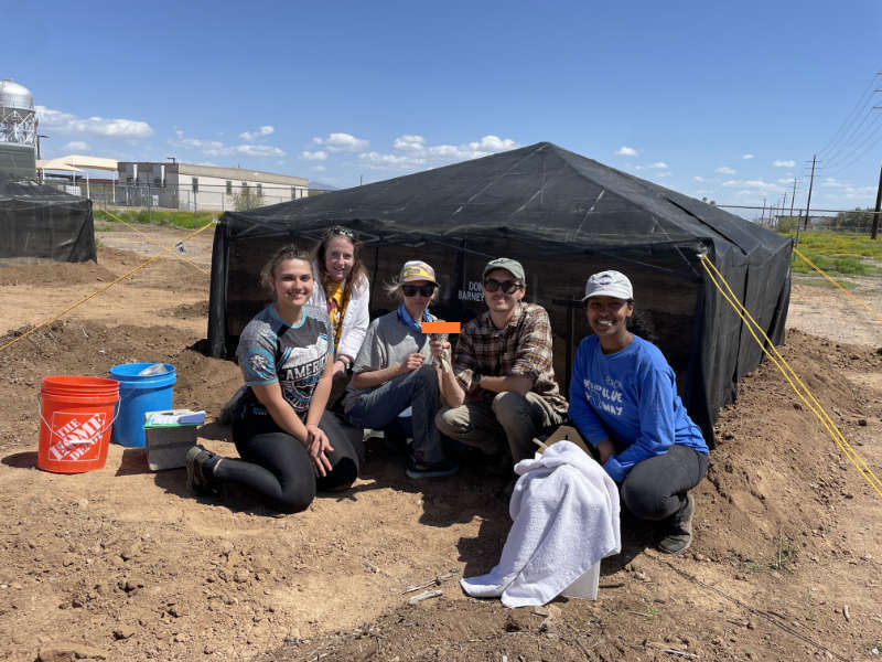 A group of five volunteers and conservationists from Wild at Heart pose in front of a newly erected tent and hold a burrowing owl up for the camera