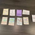 An assortment of hand-drawn cards lie on a table. Each card features a different fictional creature with a description of an exclusionary barrier.