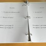 An open binder presents a page asking the reader if they prefer "Escaping into different worlds?" or "The joys of reality?" Depending on the response, the user is asked to flip to a different numbered page.