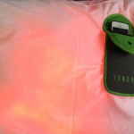 A phone sits inside a locking case on top of a pillow. A red light makes it seem like the phone is alive.